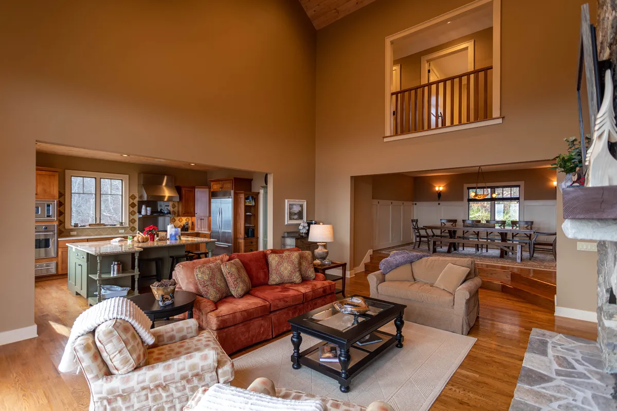A wide-angle view encompassing the kitchen island, large sectional sofa, coffee table, and dining table, all set within an interconnected open-plan living area. The kitchen island is a focal point, designed for both food prep and casual seating, while the adjacent great room and dining area promote socializing and shared experiences.