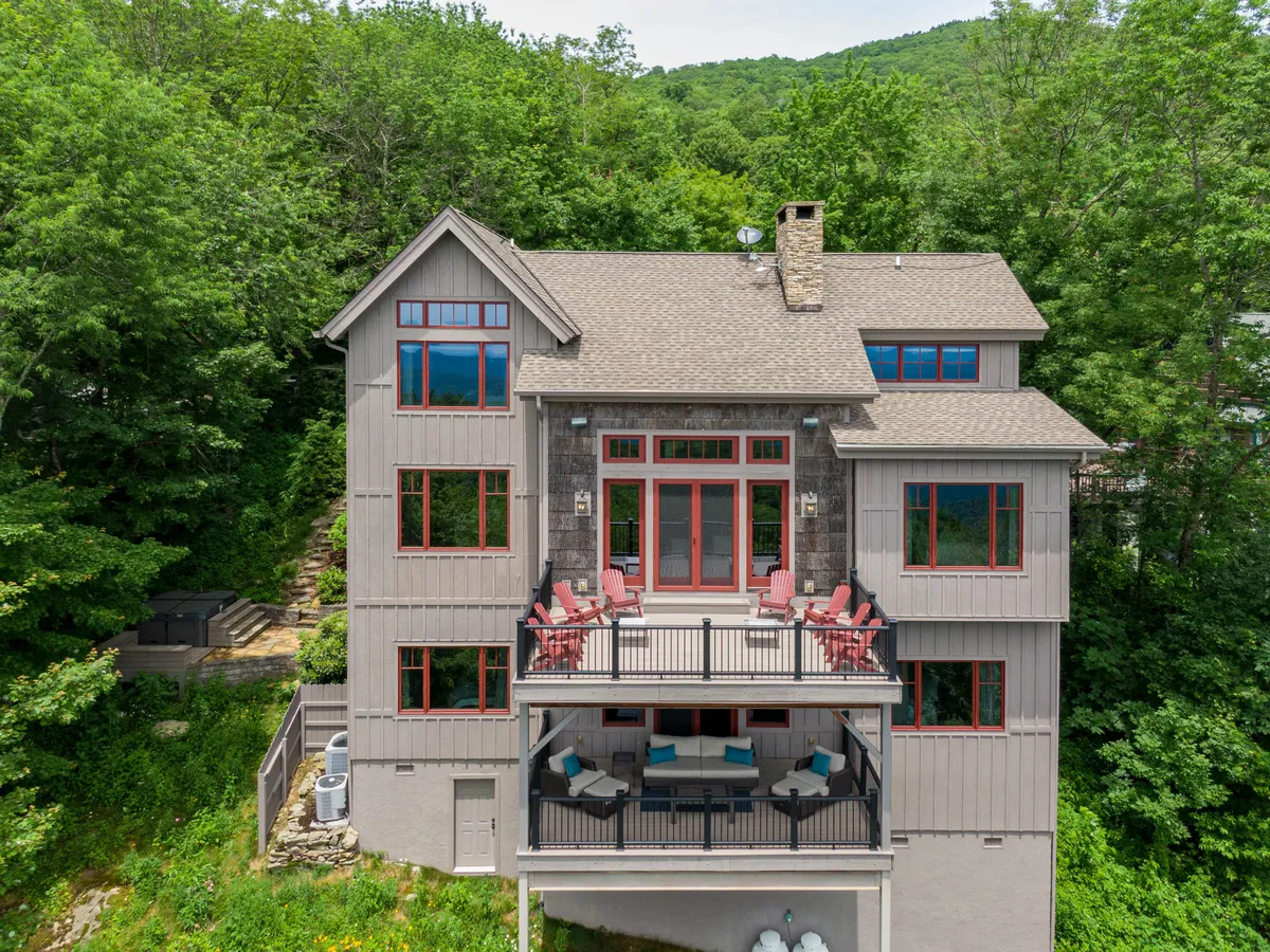 A spacious balcony overlooks vibrant greenery, with expansive windows reflecting the outdoors. The welcoming seating area on the balcony invites guests to relax, work, or enjoy a coffee break surrounded by nature, all while taking in sunset or sunrise views.