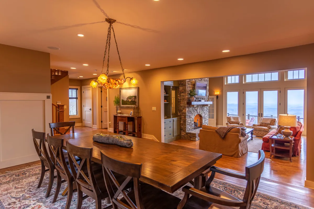 A combined living and dining space showcasing a dining table, a fireplace, and generous windows that let in natural light and frame the scenic outdoors. The room radiates a sense of coziness and connection.